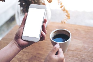 Boş masaüstü ekranı ve kafede kahve fincanı olan beyaz bir cep telefonu tutan bir kadının görüntüsü.