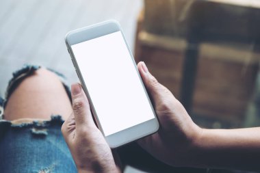 Üst görünümde, kadının elleri beyaz cep telefonunu boş ekranla tutarken görüntülendi 