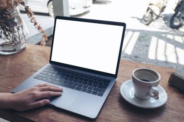 Kafedeki tahta masada boş beyaz masaüstü ekran kullanan ve laptopa dokunan bir elin görüntüsü