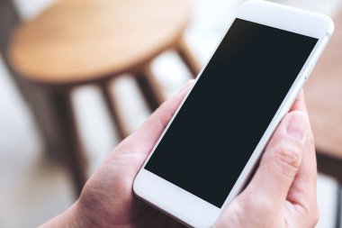 Kafede boş siyah masaüstü ekranı olan beyaz cep telefonu tutan ellerin görüntüsü