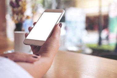 Boş masaüstü ekranı ve kafede kahve fincanı olan beyaz bir cep telefonu tutan bir kadının görüntüsü.