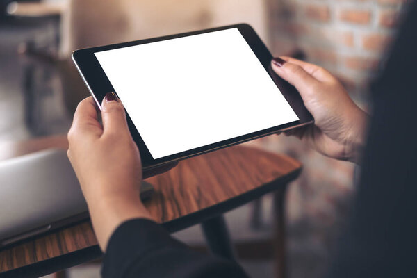 Mockup image of woman's hands holding and looking at black tablet pc with blank white desktop screen in cafe 