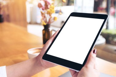 Siyah tabletli, beyaz masaüstü ekranlı, laptoplu ve kafedeki ahşap masada kahve fincanı olan kadınların ellerinin görüntüsü.