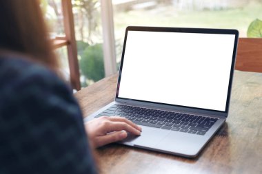 Kafedeki tahta masada boş beyaz masaüstü ekran kullanan ve laptopa dokunan bir elin görüntüsü
