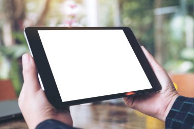 Kafe ve yeşil doğa arka planında beyaz ekranlı siyah tablet tableti tutan iş kadınının ellerinin görüntüsü.