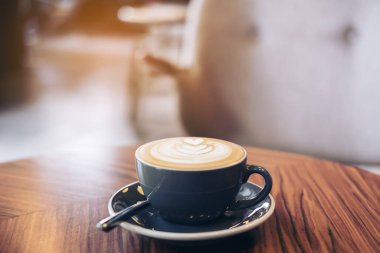 Kafedeki eski ahşap masada latte sanatıyla birlikte mavi bir fincan sıcak latte kahvenin yakın plan görüntüsü.