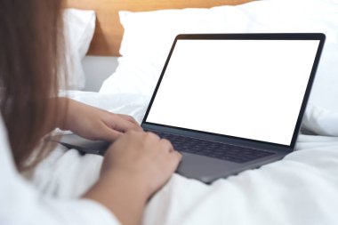 Yatağa uzanmış, boş beyaz masaüstü klavyesiyle dizüstü bilgisayarı kullanan ve yazan bir kadının görüntüsü. 