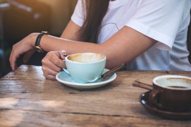 Kafedeki eski ahşap masada kahve fincanıyla kahve fincanı tutan bir kadının yakın plan görüntüsü.