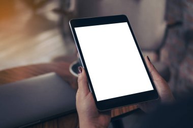 Kafedeki boş beyaz masaüstü ekranlı siyah tableti tutan kadınların ellerinin görüntüsü. 