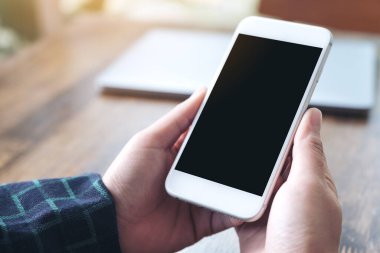 Beyaz akıllı telefonu boş siyah masaüstü ekran ve dizüstü bilgisayarla ahşap masada tutan ellerin görüntüsü. 