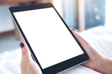 Beyaz bir yatakta otururken siyah tableti beyaz ekranla tutan kadınların ellerinin görüntüsü.