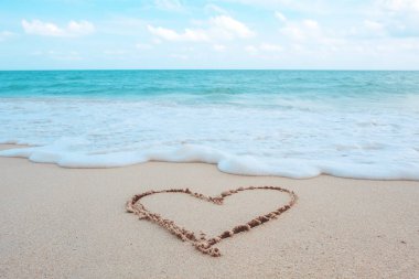 Sahilde beyaz dalgalar ve mavi gökyüzü arka planıyla kalp şeklinde el yazısı.