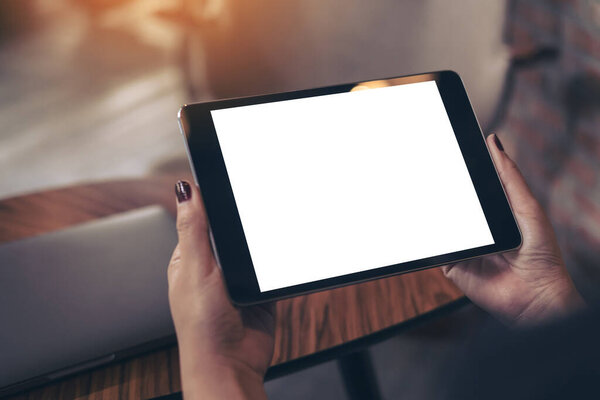 Mockup image of woman's hands holding black tablet pc with blank white desktop screen in cafe 
