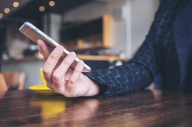 Modern kafe 'de ahşap masadaki akıllı telefonu tutan, kullanan ve ona bakan bir kadın. 