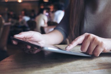 Kafe 'deki ahşap masanın üzerindeki tablet bilgisayarı gösteren, dokunan ve kullanan bir kadının yakın plan görüntüsü.