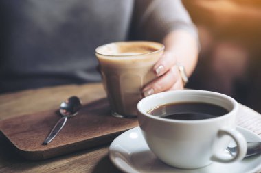 Americano kahve fincanı ve kafedeki eski ahşap masada kahve fincanı tutan kadının yakın plan görüntüsü.