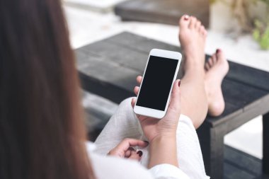 Beyaz cep telefonlu, boş siyah masaüstü ekranlı, kumlu ve plajlı bir kadının görüntüsü.