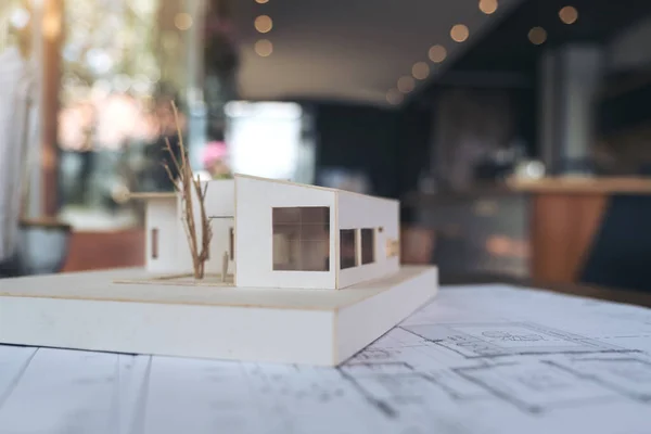 An architecture model with shop drawing paper and laptop on table in office with blur nature background