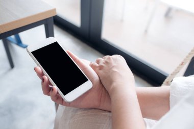 Çatı katındaki kafede beyaz cep telefonu ve boş siyah masaüstü ekranı olan bir kadının el resmi.