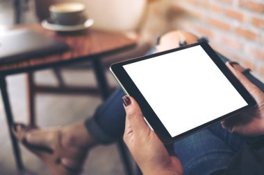 Yırtık kot pantolon giymiş, bacak bacak üstüne atmış, elinde siyah tablet bilgisayar ve boş beyaz masaüstü ekranıyla kafede oturan bir kadının en üst görüntü görüntüsü.