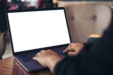 İş kadınının laptopta boş beyaz masaüstü ekran ve kafedeki ahşap masada kahve fincanı kullanarak ve yazarak görüntüsü.