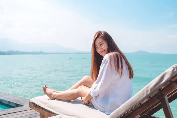 一个穿着白色衣服的快乐美丽的亚洲女人坐在蓝天背景的海床上的画像 — 图库照片