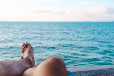 Mavi gökyüzü arka planına sahip deniz kenarında otururken insanın bacakları ve ayağının yakın görüntüsü.