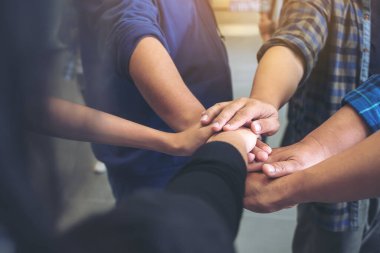 İş ekibinin ayakta ve ofiste el ele tutuşurken yakın plan görüntüsü. 