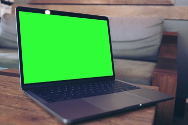 Modern çatı katındaki ahşap masa üzerinde boş yeşil masaüstü ekranlı dizüstü bilgisayarın görüntüsü