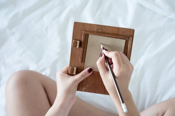 A woman writing on a brown paper with wooden writing pad on the bed
