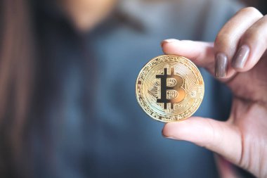 Ofiste elinde altın rengi bir Bitcoin tutan ve gösteren bir iş kadını resmi