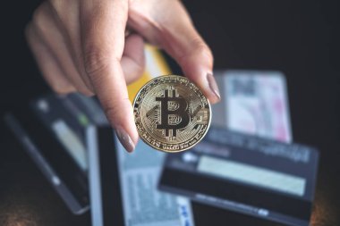 Ofisinde bir sürü kredi kartı olan altın renkli bir Bitcoin tutan bir kadının yakın plan görüntüsü.