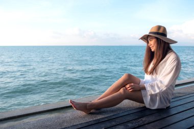 Beyaz elbiseli mutlu bir Asyalı kadının portresi. Deniz kenarındaki ahşap balkonda, açık mavi arka planda oturuyor.