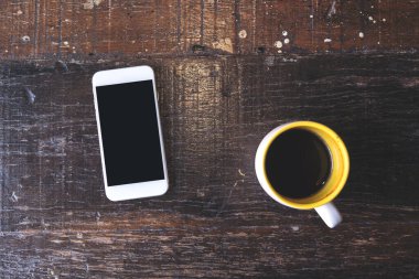 Üst görünüm görüntüsü beyaz bir cep telefonunun boş siyah masaüstü ekran ve kahve fincanı ile klasik ahşap masa. 