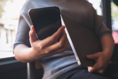 Bilgisayarı elinde tutarken akıllı telefonu kullanan ve ona bakan bir kadının yakın plan görüntüsü