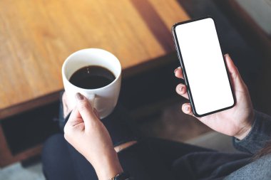 Kafede kahve içerken beyaz ekranlı siyah cep telefonu tutan bir kadının görüntüsü.