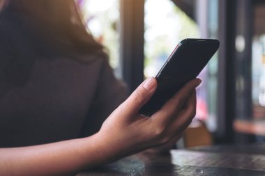 Bir el ele tutuşmanın ve kafede siyah akıllı telefon kullanmanın yakın plan görüntüsü.