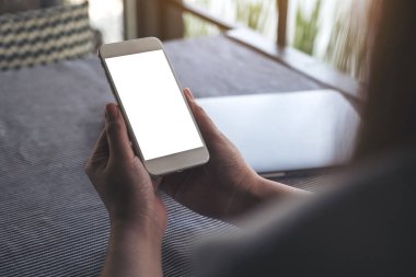 Boş masaüstü ekranı ve kafedeki masada dizüstü bilgisayarı olan beyaz cep telefonunu tutan ellerin görüntüsü