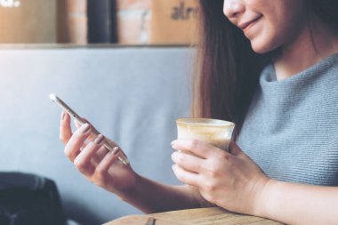 Kafede kahve içerken elinde akıllı telefon tutan ve kullanan Asyalı güzel bir kadının yakın plan görüntüsü.
