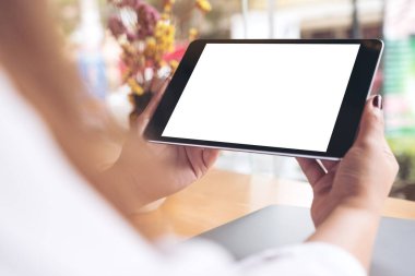 Siyah tabletli, beyaz masaüstü ekranlı, laptoplu ve kafedeki ahşap masada kahve fincanı olan kadınların ellerinin görüntüsü.