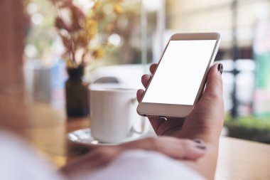 Boş masaüstü ekranı ve kafede kahve fincanı olan beyaz bir cep telefonu tutan bir kadının görüntüsü.