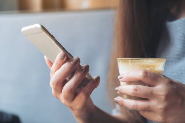 Kafede kahve içerken akıllı telefon kullanan ve el ele tutuşan bir kadının yakın plan görüntüsü.