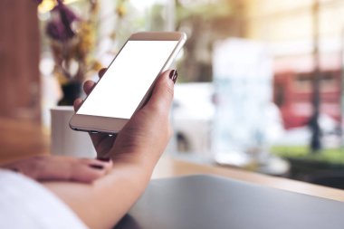 Boş masaüstü ekranı ve kafede kahve fincanı olan beyaz bir cep telefonu tutan bir kadının görüntüsü.