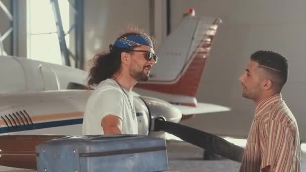 Колумбийский гангстер в белой рубашке в стиле 80-х стоит рядом с самолетом и проверяет качество кокаина или других наркотиков, держит пулемет, очень серьезный, недоверчивый — стоковое видео