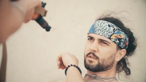 Der kolumbianische Gangster hält eine Schusswaffe in der Hand, oben ohne, droht mit einer Maschinenpistole, zielt auf eine Person, ist aggressiv, will töten, die Handlung spielt sich am Strand ab — Stockvideo