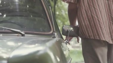 Genç bir adam 80 lerin tarzında yürüyüşler SSCB kez eski Sovyet yeşil araba yakınındaki giyinmiş, o mesafe içine bakar, arabaya girer ve kapıyı açar