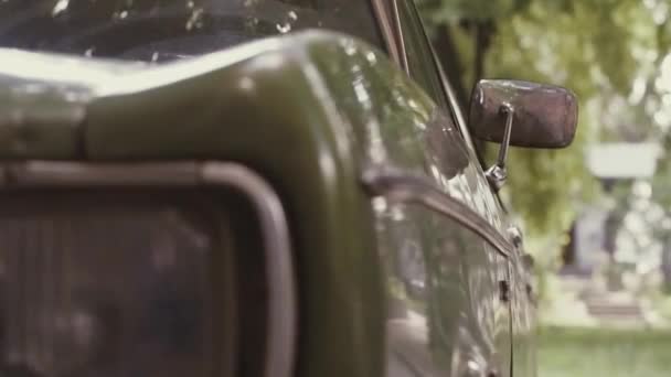 Молодой человек в стиле 80-х идет рядом со старым советским зеленым автомобилем времен СССР, заглядывает вдаль, идет к машине и открывает дверь — стоковое видео