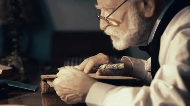 Een oude zanger werkt in zijn creatieve studio, een getextureerd schrijver in stijlvolle retro kleding, een grijs-haired bebaarde man, bladeren door middel van een notebook, schrijft gedichten en een boek op een typemachine — Stockvideo