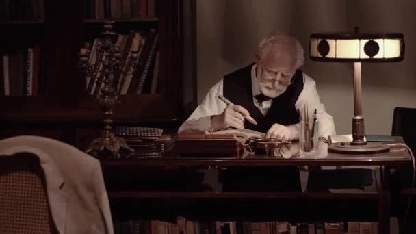 Un vieux chanteur travaille dans son atelier de création, un écrivain texturé dans des vêtements rétro élégants, un homme barbu aux cheveux gris, feuillette un carnet, écrit des poèmes et un livre sur une machine à écrire — Video