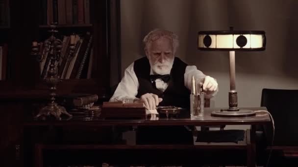 Un vieux chanteur travaille dans son atelier de création, un écrivain texturé dans des vêtements rétro élégants, un homme barbu aux cheveux gris, feuillette un carnet, écrit des poèmes et un livre sur une machine à écrire — Video
